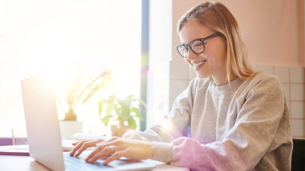 Lady With Glasses Smiling While Typing On Her Laptop